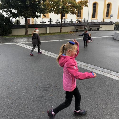 Die Kinder balancieren Körnerkissen auf ihrem Kopf und bewegen sich wie Luftballons über die Fläche.